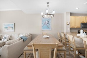 A modern kitchen with wooden cabinets, a dining table with chairs, a chandelier, and a painting of an octopus on the wall.