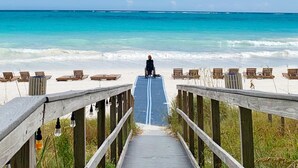 A wooden boardwalk leading to a beach with lounge chairs and a person in a wheelchair. - Grandview East 1601 - Azure Paradise (Panama City Beach)