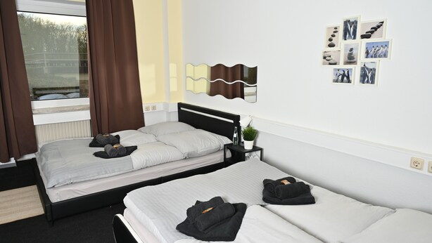 Habitación de hotel con dos camas, una ventana con cortinas, un espejo colgado en la pared y una pequeña planta.