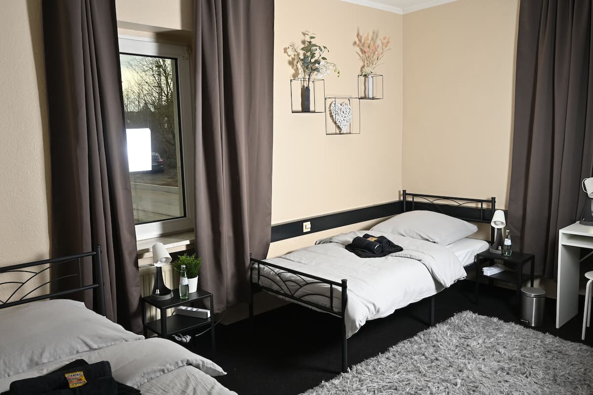 A bedroom with two beds, a window with curtains, a bedside table with a lamp, and wall-mounted decorations.