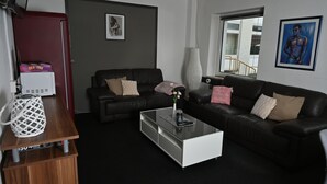 Una sala de estar moderna con un sofá de cuero negro, una mesa de centro blanca y una mesita de noche de madera con una cesta trenzada blanca.
