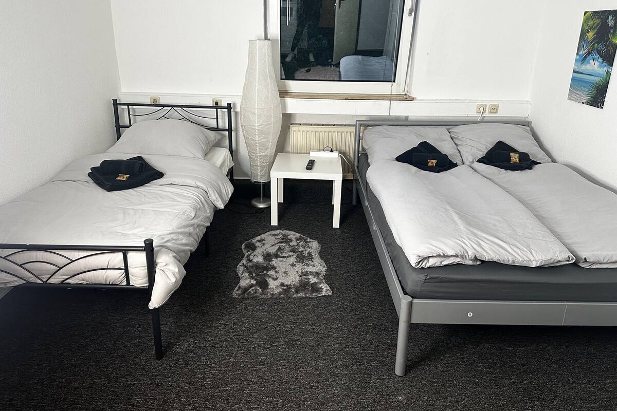 A small, compact room with two single beds, a small table, a radiator, and a window.