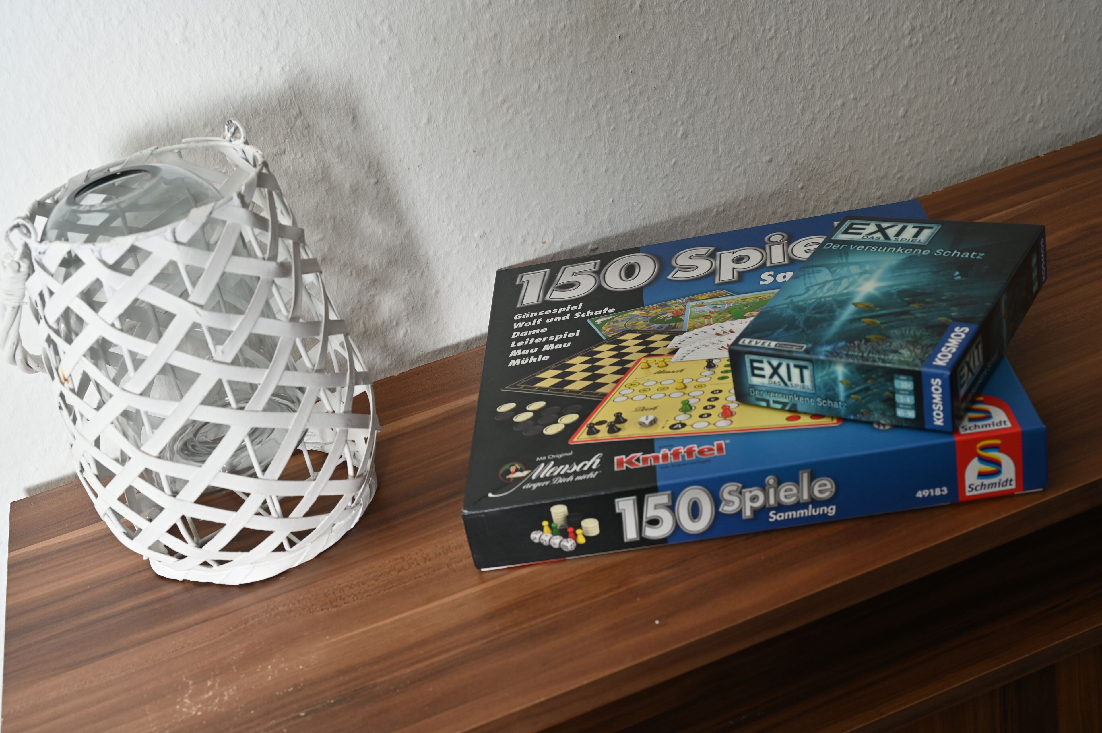 A box of 150 Spiele board game and a white woven basket on a wooden surface.