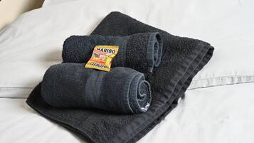 Toalha cinza escura, dobrada com cuidado, com etiqueta Haribo Goldbären sobre uma cama branca.
