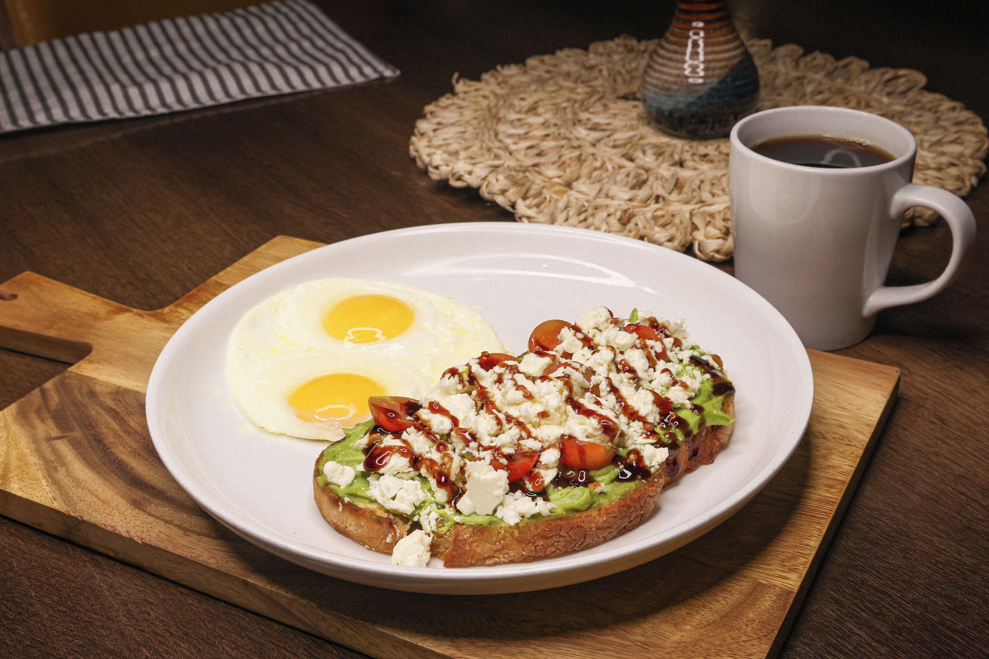 Ein Teller mit einem Frühstückssandwich und zwei Spiegeleiern auf einer Holzplatte.
