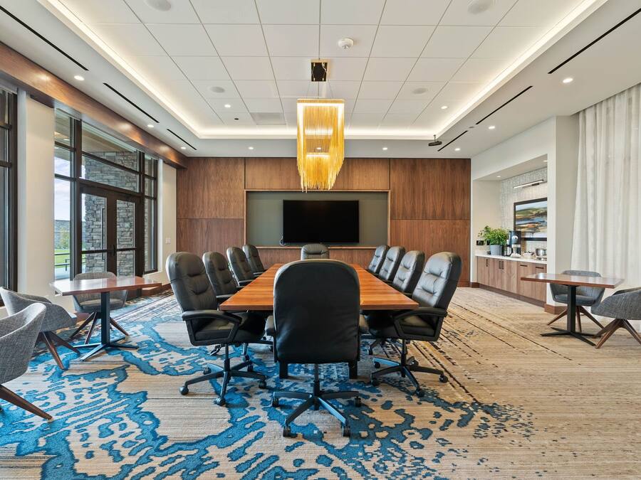 A modern conference room with a long table, comfortable chairs, a large screen, and a view of the outdoors.