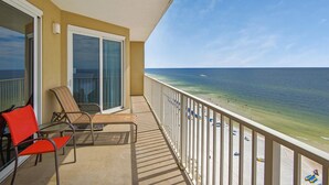 A balcony with a view of the beach, a chair, and a table.