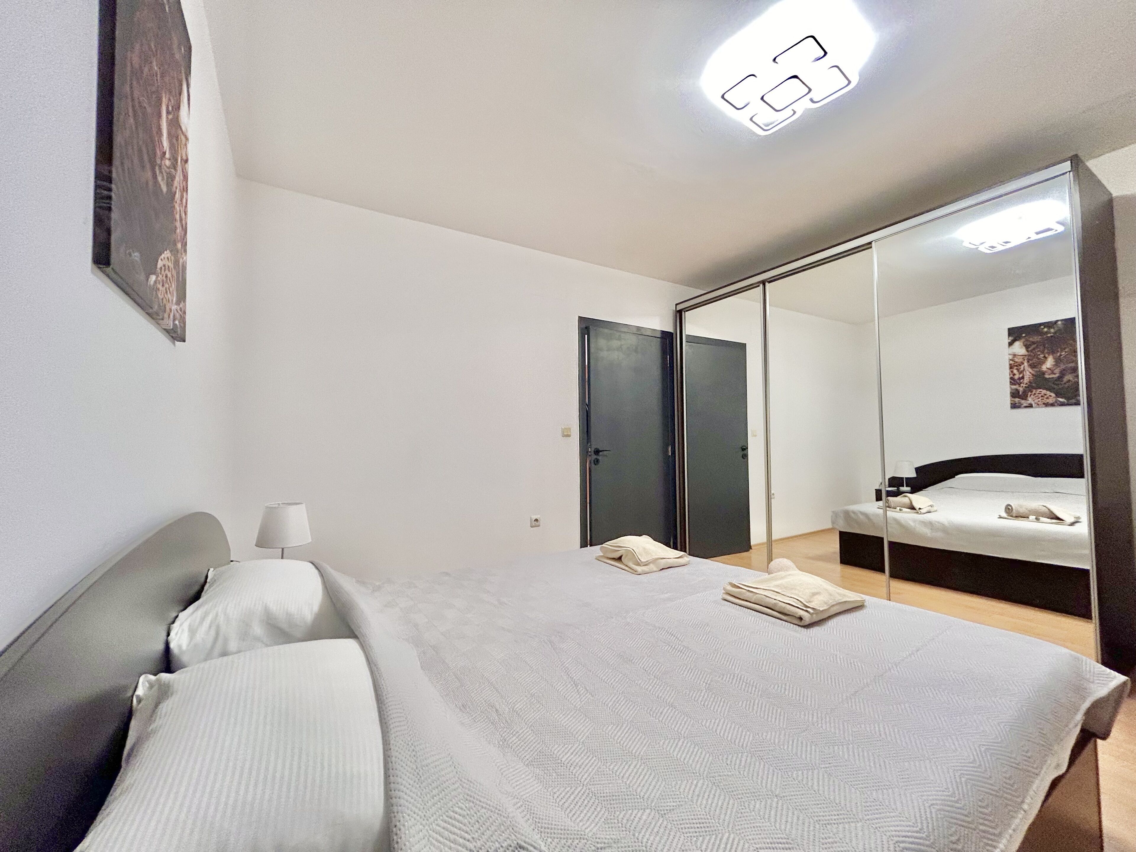 A bedroom with a bed, bedside lamps, a large mirror, and a ceiling light.