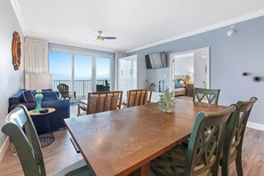 A spacious dining area with a wooden table and chairs, a blue sofa, and a balcony with a view.
