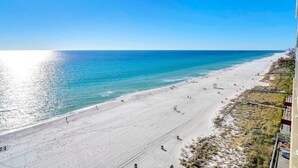 Ein Strand mit blauem Himmel, einem Steg in der Ferne und einem Gebäude auf der rechten Seite.