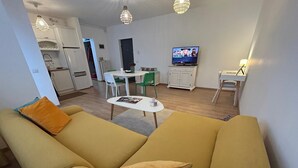 A living room with a yellow sofa, a small round table, and a television in the background. - Serelor Apartment Free Parking (Dumbrăvița)
