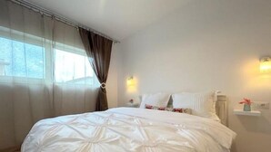 A neatly made bed with a white duvet, a bedside table with a lamp, and a window with curtains. - Serelor Apartment Free Parking (Dumbrăvița)