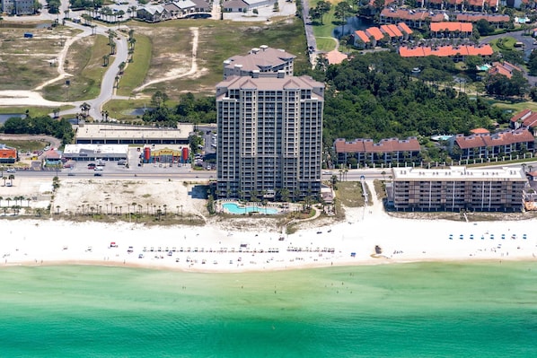 A high-rise hotel with a pool, beachfront, and adjacent residential buildings.