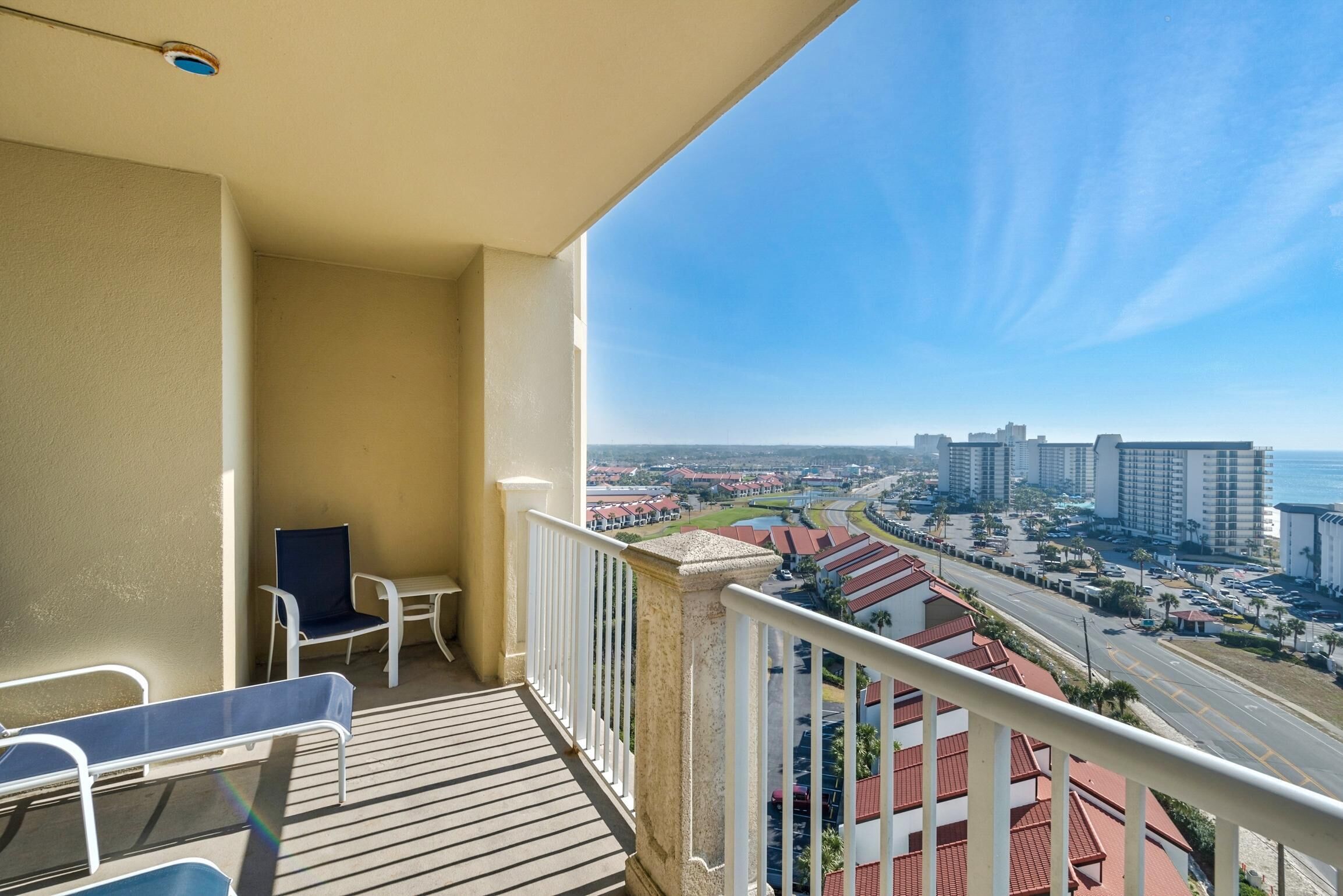 A balcony with a view of a coastal cityscape, including buildings and a road.