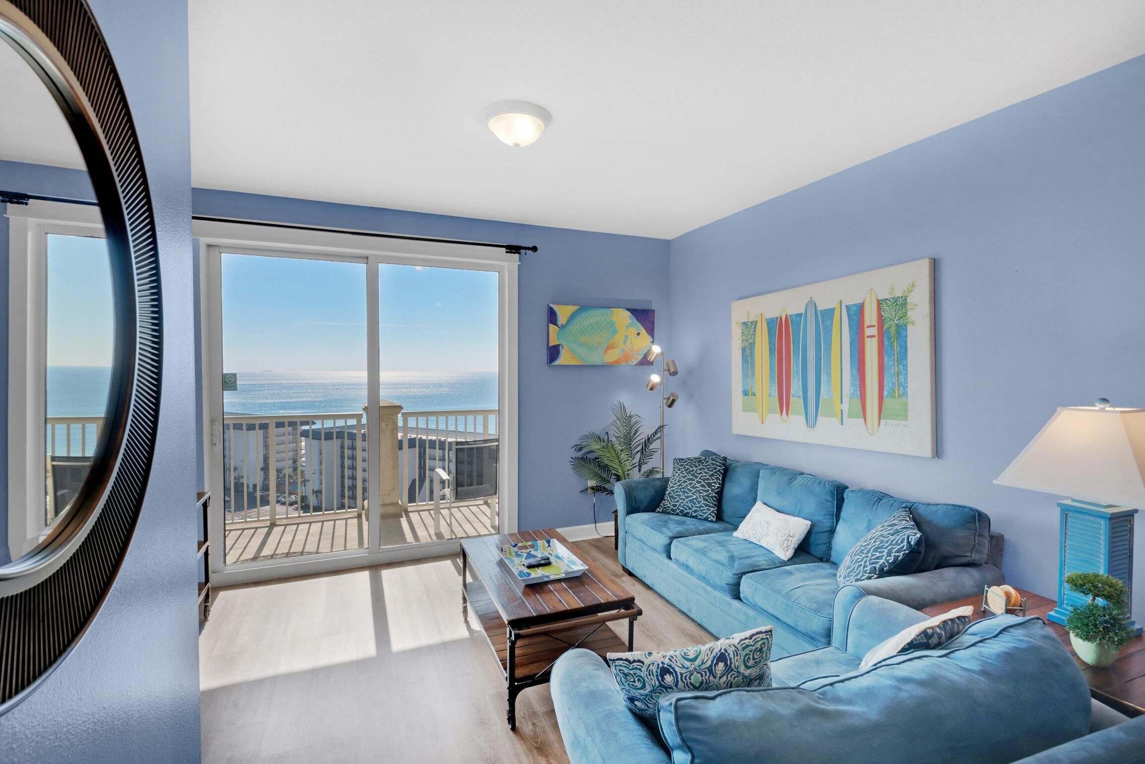 A living room with a blue sofa, a coffee table, and a view of the ocean through a sliding door.
