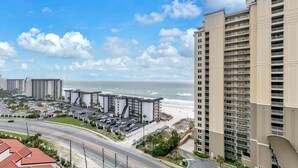 A coastal hotel with multiple floors, a parking lot, and a beach view.