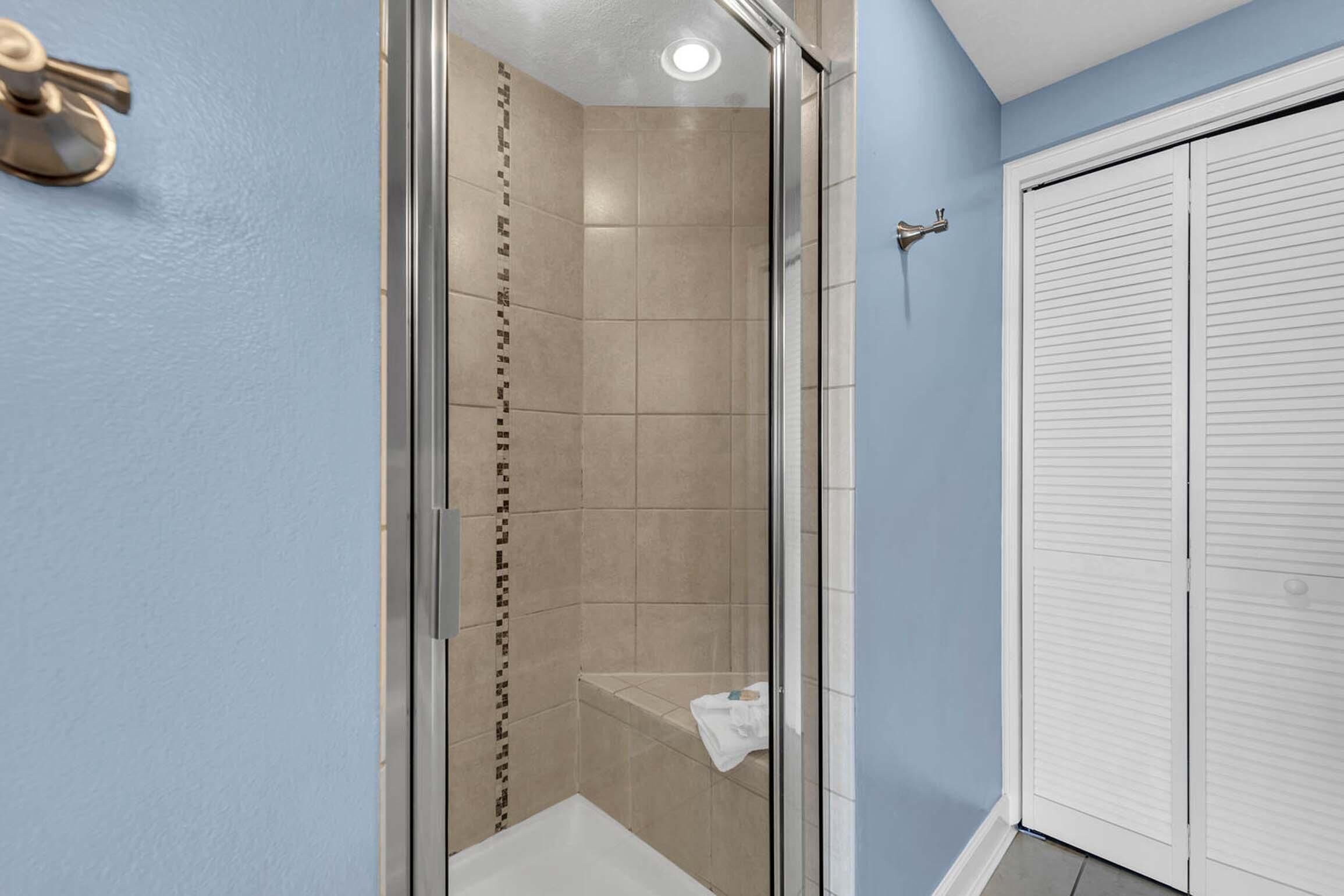 A bathroom with a glass shower enclosure, beige tiles, and a white toilet.