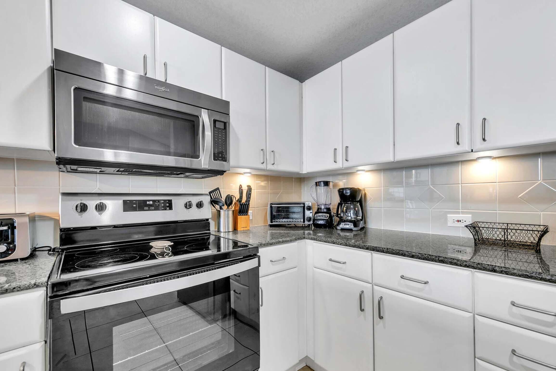 A modern kitchen with white cabinets, stainless steel appliances, and a granite countertop.