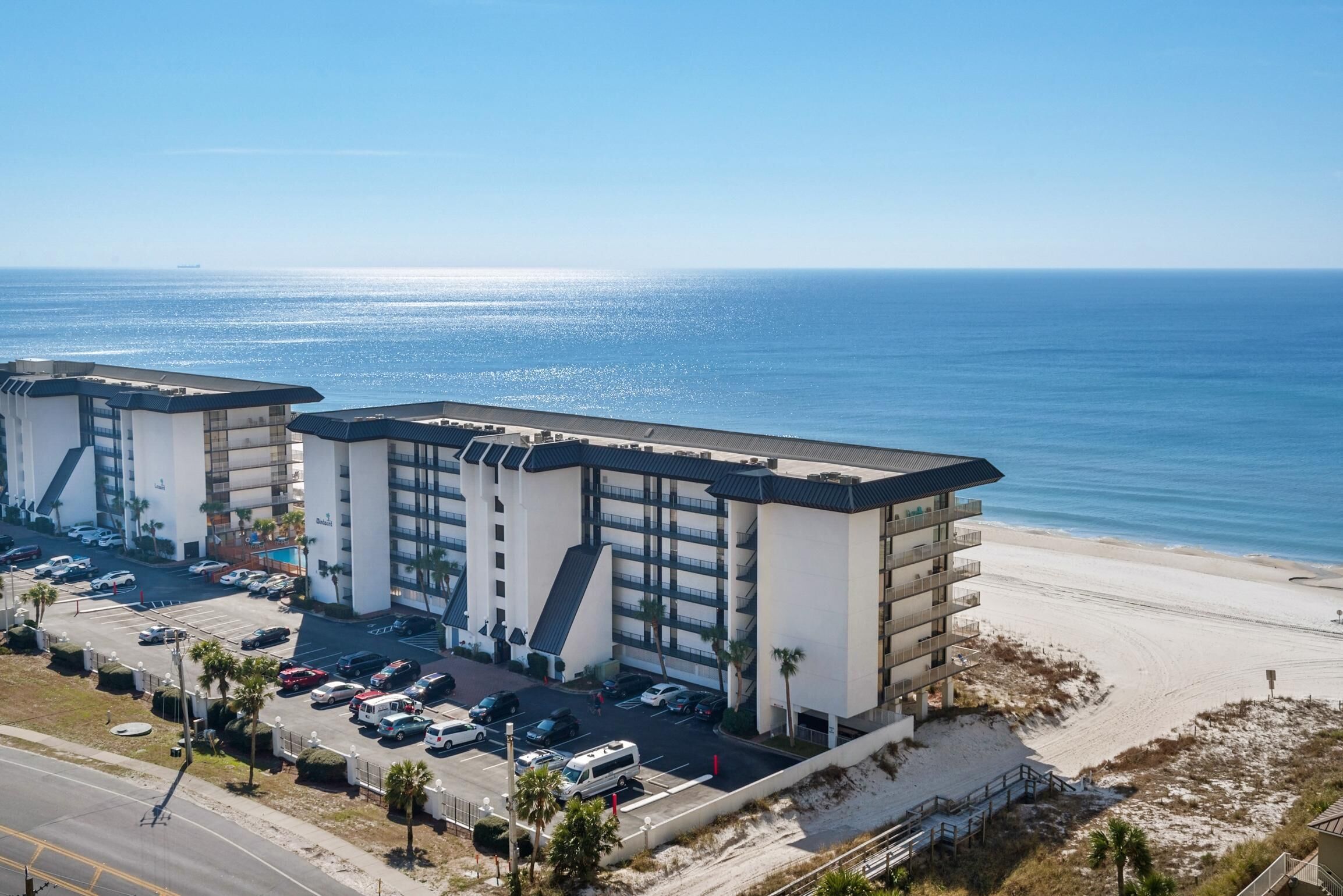A beachfront hotel with multiple floors, a parking lot, and a view of the ocean.