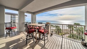 Ein Balkon mit Holztisch und -stühlen, mit Blick auf Strand und Meer.
