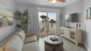 A living room with a sofa, a coffee table, a TV, and a balcony with a view of the ocean.