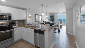 A modern kitchen with stainless steel appliances, a granite countertop, and a view of the ocean through large windows.