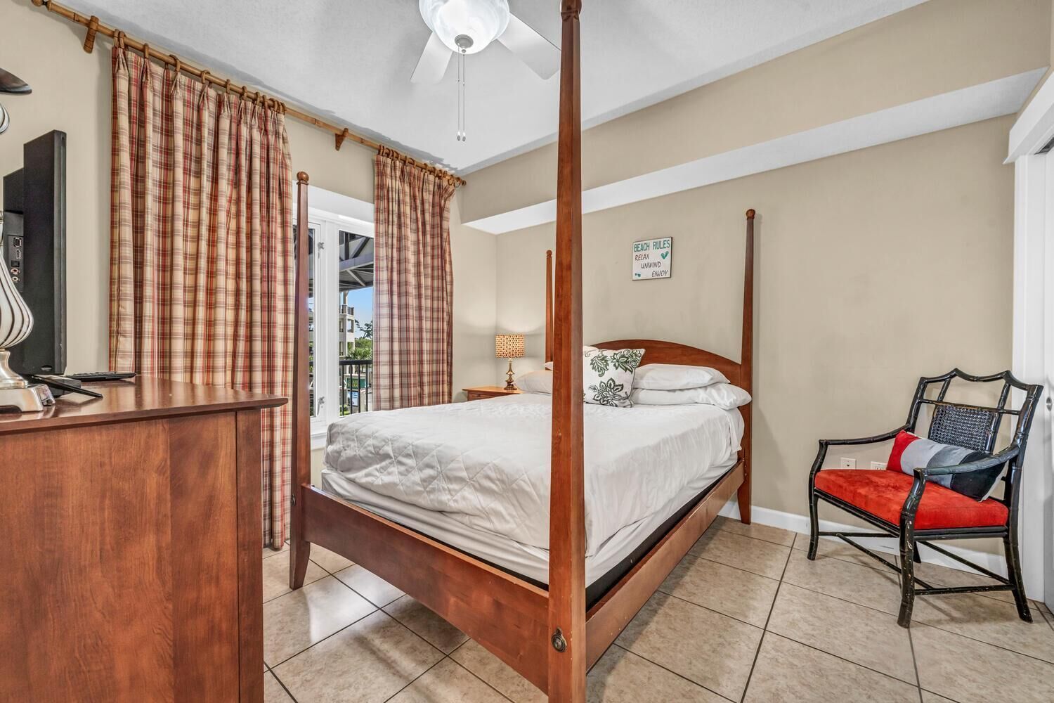 A four-poster bed with a wooden frame, a desk with a lamp, and a chair with a cushion.