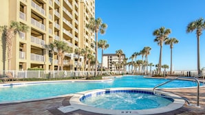 A hotel pool area with a hot tub, palm trees, and a building with balconies. - Grand Panama 1-1401 (Panama City Beach)