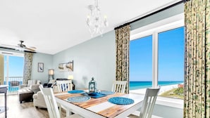 A dining area with a view of the ocean, a chandelier, and a table with blue placemats. - Grand Panama 1-1401 (Panama City Beach)