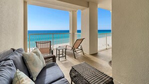 A balcony with a view of the ocean, furnished with a sofa, chairs, and a small table. - Grand Panama 1-1401 (Panama City Beach)