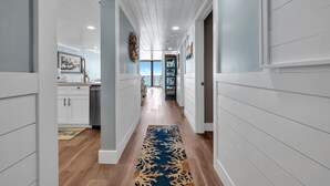 A hallway with white paneled walls, a wooden floor, and a blue patterned rug. - Edgewater Tower 3-412 (Panama City Beach)