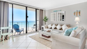 A modern living room with a white sofa, a coffee table, and a view of the ocean through large sliding doors. - Edgewater Tower 2-408 (Panama City Beach)