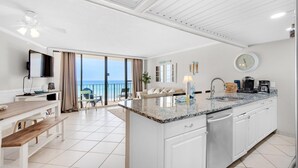 A modern kitchen with a large island, white cabinetry, and a view to the outside. - Edgewater Tower 2-408 (Panama City Beach)