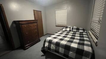 A bedroom with a bed, a dresser, a window with blinds, and a door.
