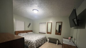 Une chambre à coucher avec un lit, un bureau, un miroir et une télévision.