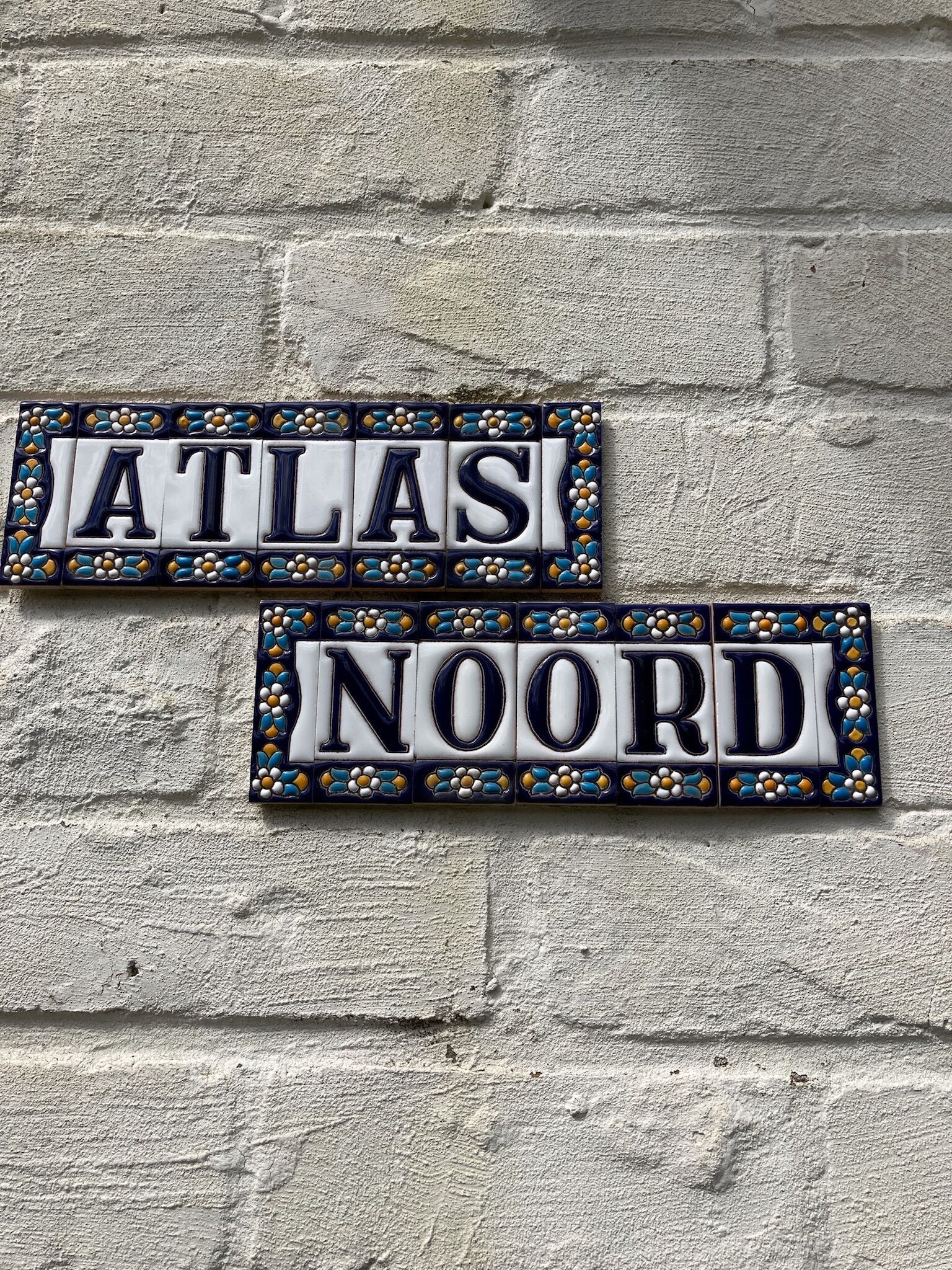 Two rectangular signs with decorative borders and the words "ATLAS" and "NOORD" on a textured wall.