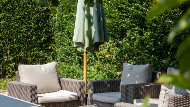 Un espace extérieur aménagé avec des meubles en osier et une table, le tout entouré d’une végétation luxuriante.