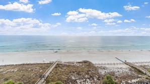 A beach with a wooden walkway leading to the shore, a clear sky, and calm sea. - Indigo West 804 (Pensacola)