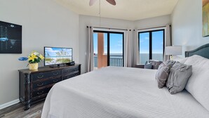 Une chambre d’hôtel avec un grand lit, un ventilateur de plafond, une télévision, une commode et un balcon avec vue.