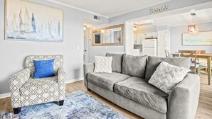 A living room with a patterned armchair, a grey sofa, and a blue rug. - The Place To Be II (Myrtle Beach)