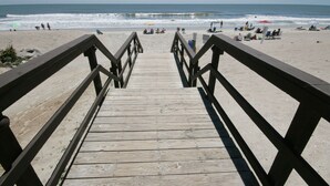 A wooden boardwalk leading to a beach with people and umbrellas. - The Place To Be II (Myrtle Beach)