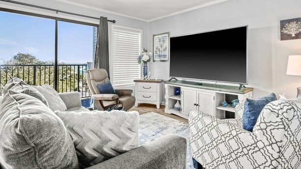 A modern living room with a large TV, comfortable seating, a small side table, and a balcony with a view. - The Place To Be II (Myrtle Beach)