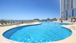 A large, clear swimming pool with a sandy deck, surrounded by a high-rise building and a fenced area. - The Place To Be II (Myrtle Beach)