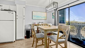 A compact kitchen with a refrigerator, a dining table with chairs, and a view of the outdoors through a large window. - The Place To Be II (Myrtle Beach)