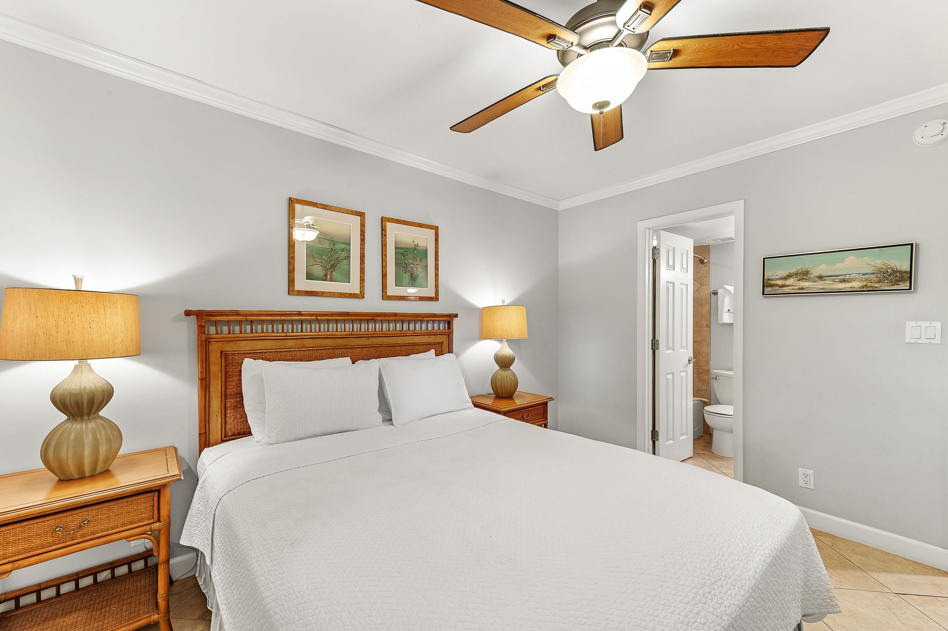 A bedroom with a wooden headboard, two bedside lamps, a ceiling fan, and a door leading to a bathroom.