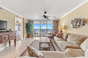 A spacious living room with a sofa, a coffee table, and a TV. There is a balcony with a view of the sky and a plant.