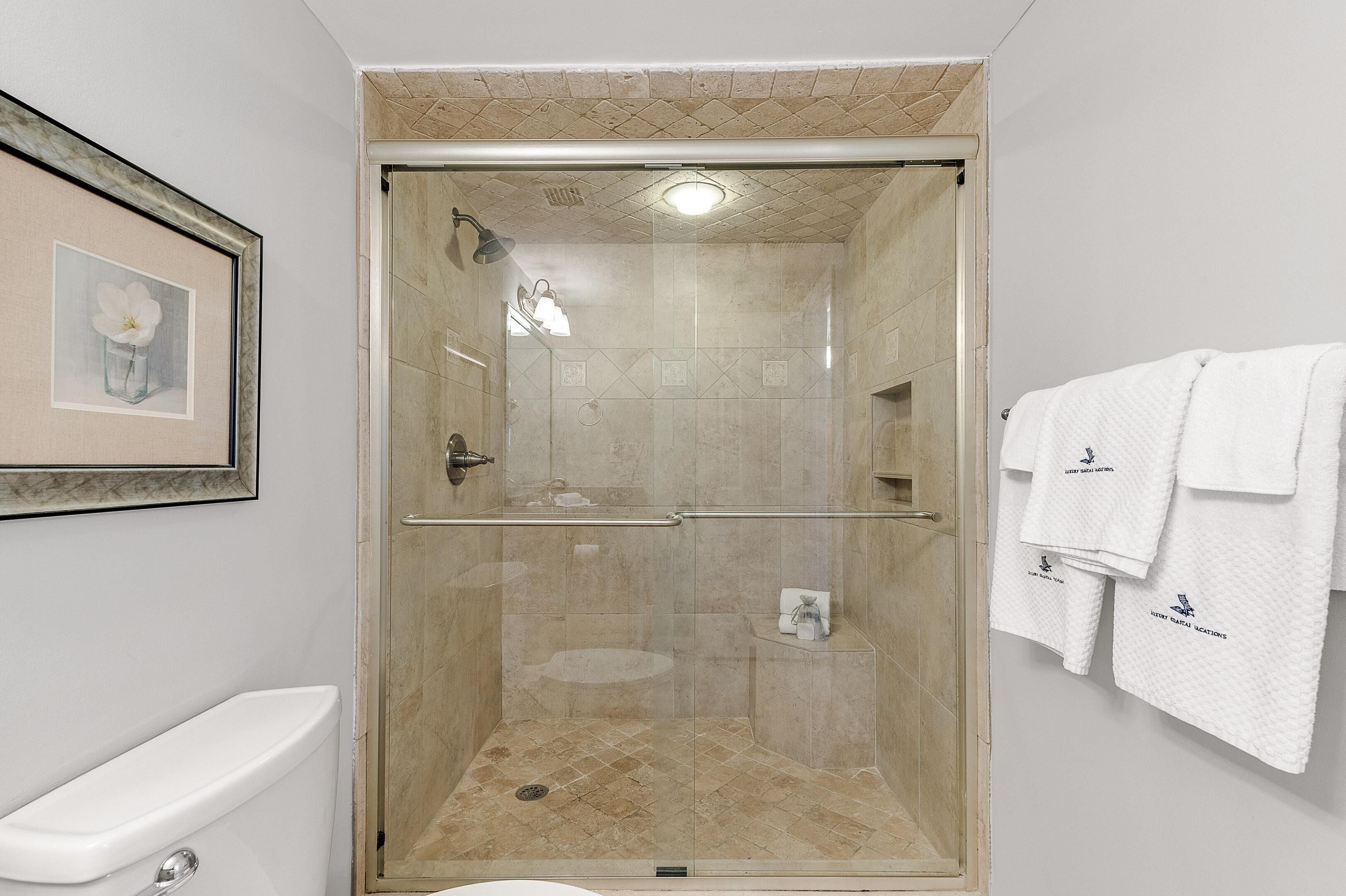 Een douche met glazen wand, een betegelde vloer, een toilet en een ingelijst schilderij aan de muur.