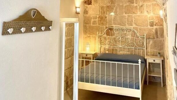 Un dormitorio con techo de piedra, una cama con estructura metálica, una mesita de noche y un perchero en la pared.