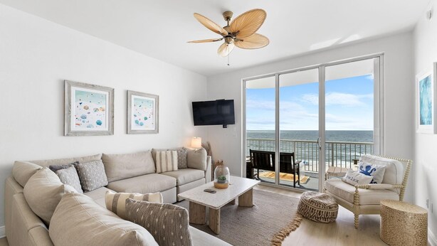 A spacious living room with a large window offering a view of the ocean, a ceiling fan, and a flat-screen TV mounted on the wall. - Spanish Key 603 (Pensacola)