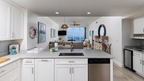 A modern kitchen with white cabinetry, a central island with a sink, and a view to the living area. - Spanish Key 603 (Pensacola)